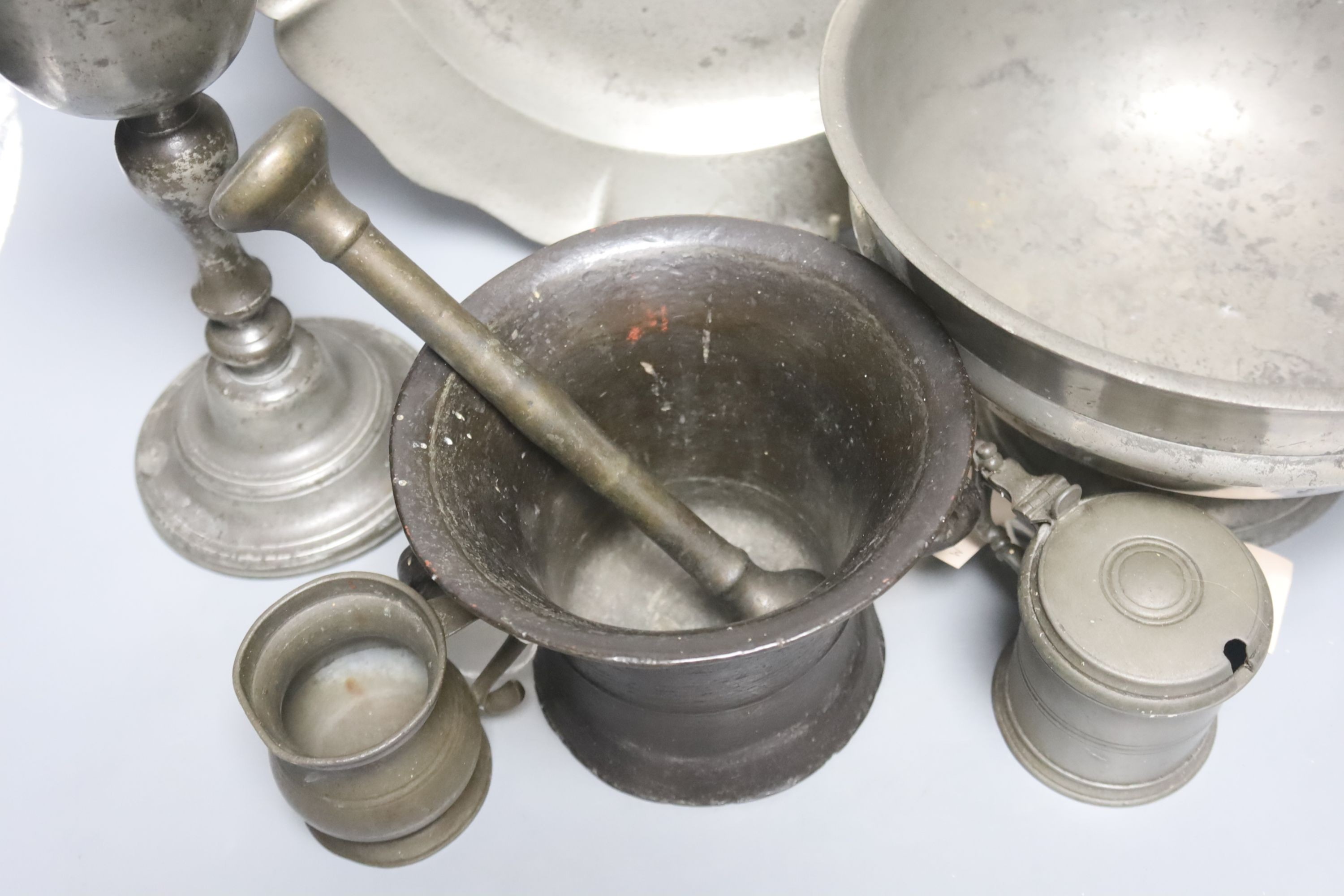 A pewter pedestal bowl, a barbed and crested dish, three other items of pewter and a 17th/18th century bronze pestle and mortar